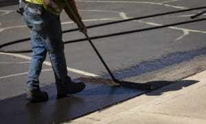 Worker using a sealcoating brush during asphalt resurfacing project